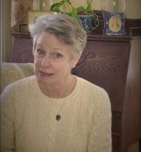 Jill Mueller reads a speech by Marmee in Louisa May Alcott's "Little Women" for Mother's Day. She has short gray hair, pale skin, and is wearing a yellow sweater.